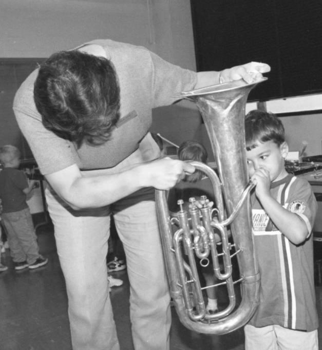 An adult holds a tuba while a child tries to blow into it.