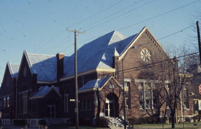 A Romanesque Revival building with detailing including terra cotta insets, wheel windows, round arch and jack arch lintels.