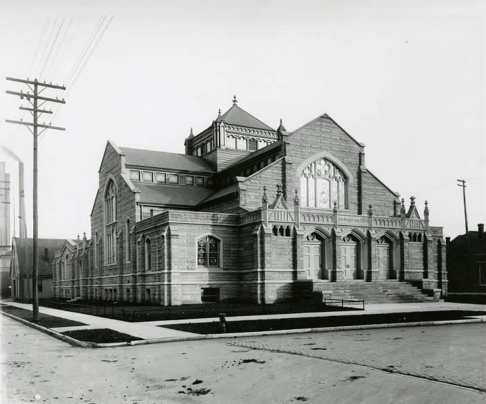 A large ornate church building on the corner of a street. The entrance has three separate doors.