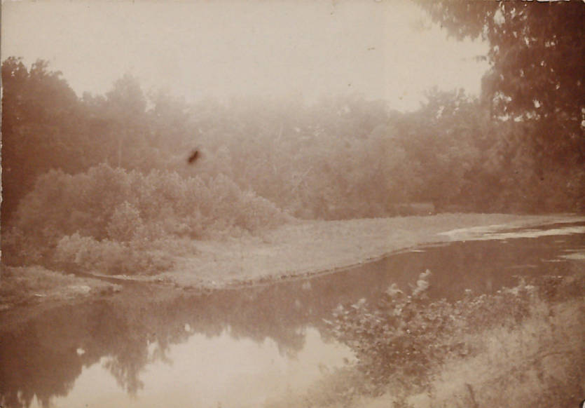 A faded photograph shows a river between shrub and tree lined banks.