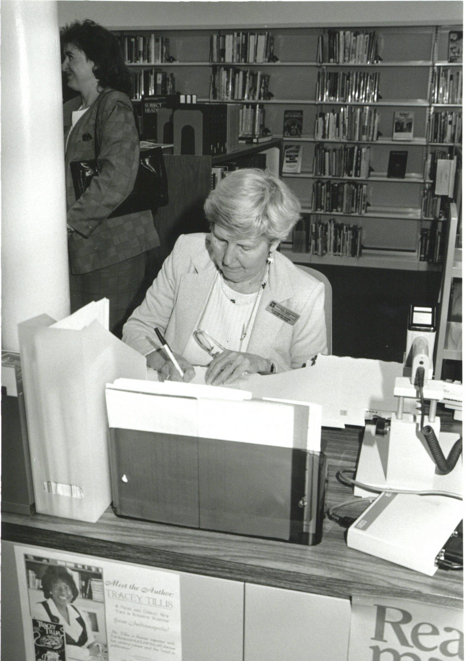 A woman sits at a desk and is writing.