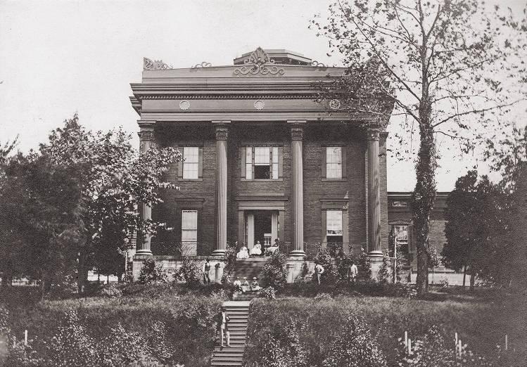A square, two-story Greek revival mansion with four columns supporting a decorative pediment across the front of the house. It has ornamental pediments over the windows and doors.