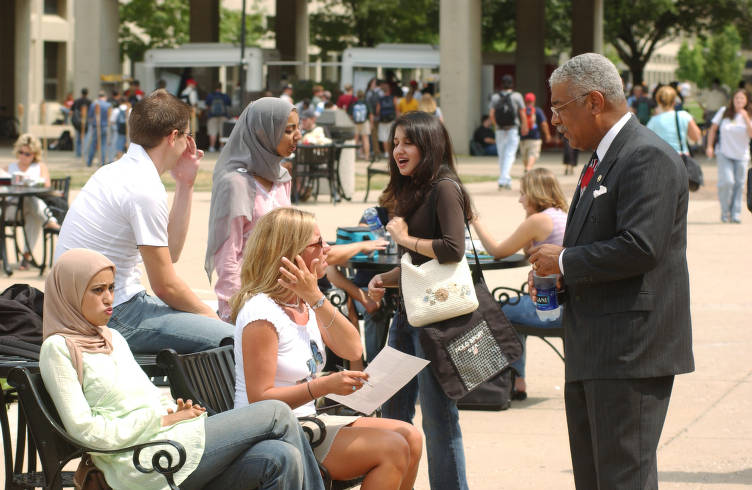 Frank Anderson talks to several students who are sitting outside on a bench. 