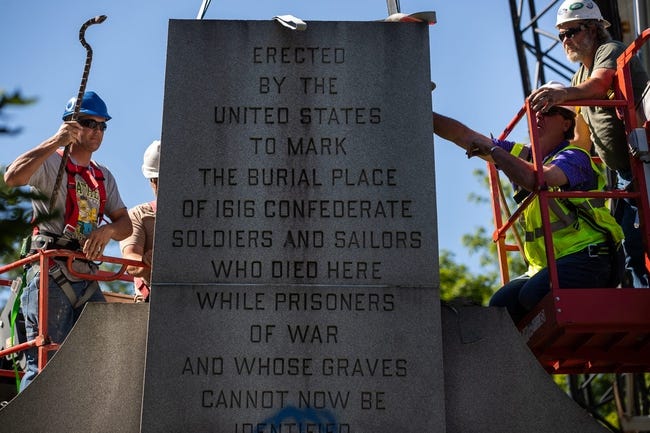 Four workers in bucket lifts work together to remove a monument. 