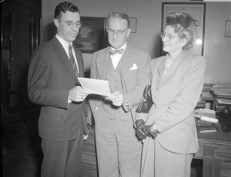 Two men and a woman stand together looking at a document.