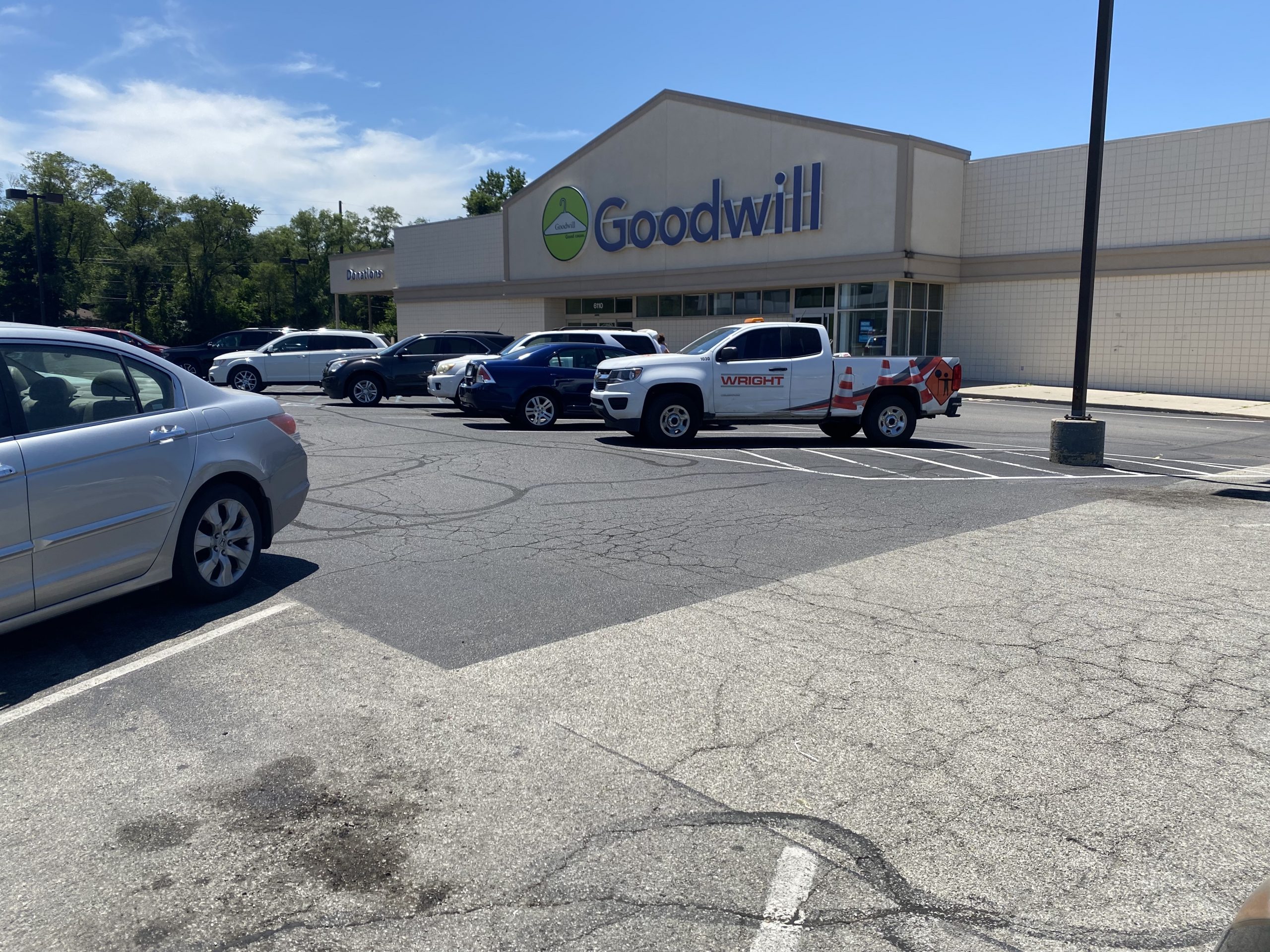 A view of the entrance of a Goodwill building. The parking lot in the front of the building is full of cars. 