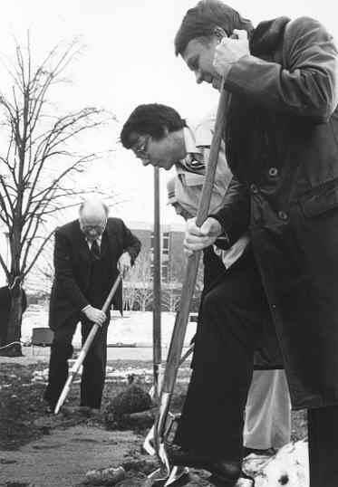 Three people hold shovels and dig into the ground.