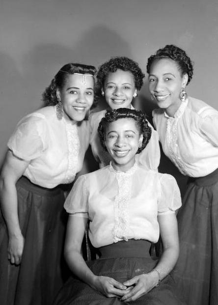 A group of four young women wear matching blouses and skirts.