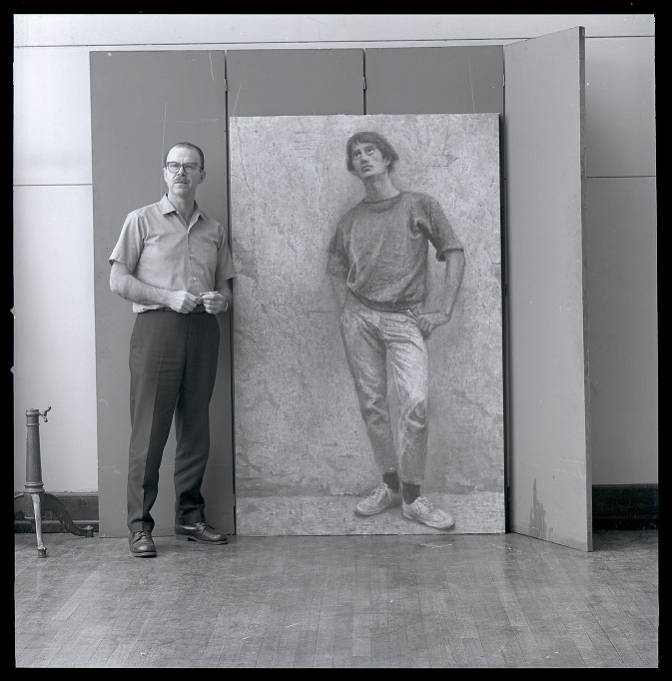 The artist stands next to a life-size painting of a young man.
