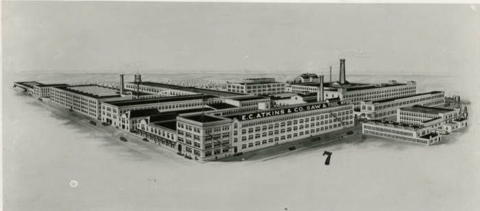 Pen and ink rendering of a sprawling series of connected, industrial-looking buildings. The buildings are two to four stories high and three have smokestacks.