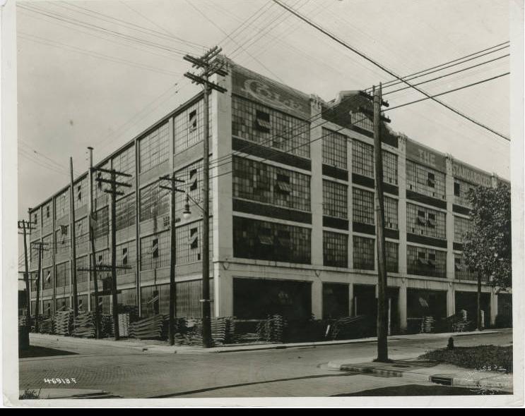 	 View of the Cole Motor Car Co. building which is mostly glass. Stacks of materials surround the building.