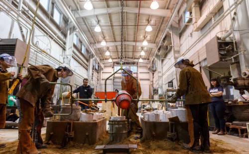 Several people work an apparatus to pour something molten hot. All individuals are wearing protective gear.
