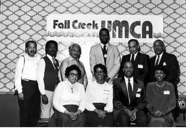 A group of people stand together in front of a wall with a sign that reads "Fall Creek Y M C A."
