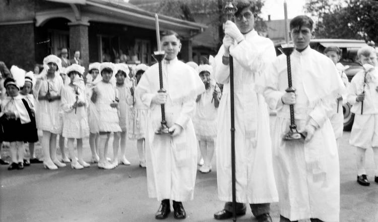 Several boys in white robes hold candles. Younger children stand behind them holding flowers.