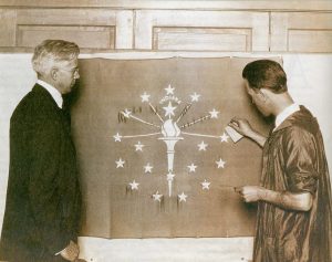 Paul Hadley, designer of the Indiana state flag, looks on as a Herron Art Institute student applies gold leaf to the original flag presented to the state, ca. 1923