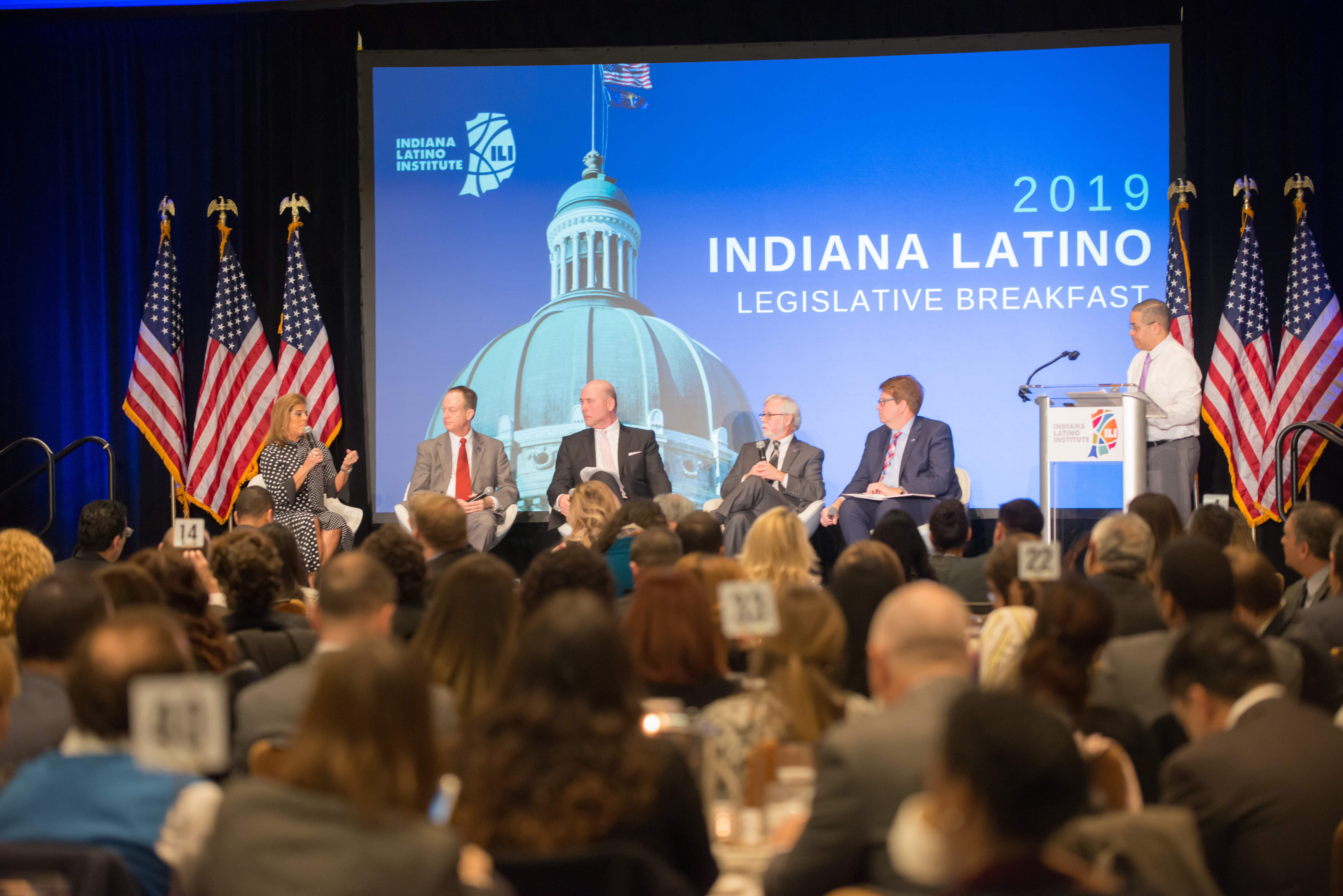 A panel of people sit on a stage in front of an audience. 