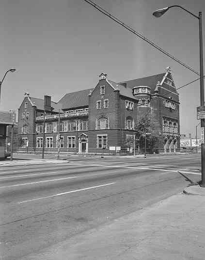 An exterior view of a 3 1/2-story rectangular building with extensive trim and decoration. In overall impression, the building is eclectic showing German or Bavarian adaptations of Romanesque, Greek, and Gothic detailing.