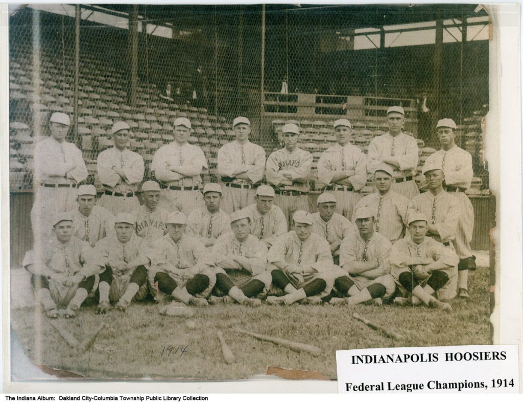 Three rows of baseball players are grouped in front of the backstop of a baseball diamond.