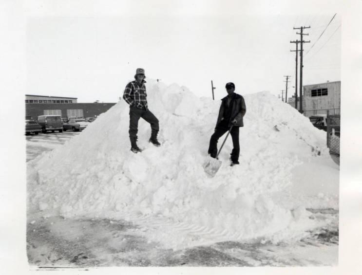 Two people stand on top of a large pile of snow.