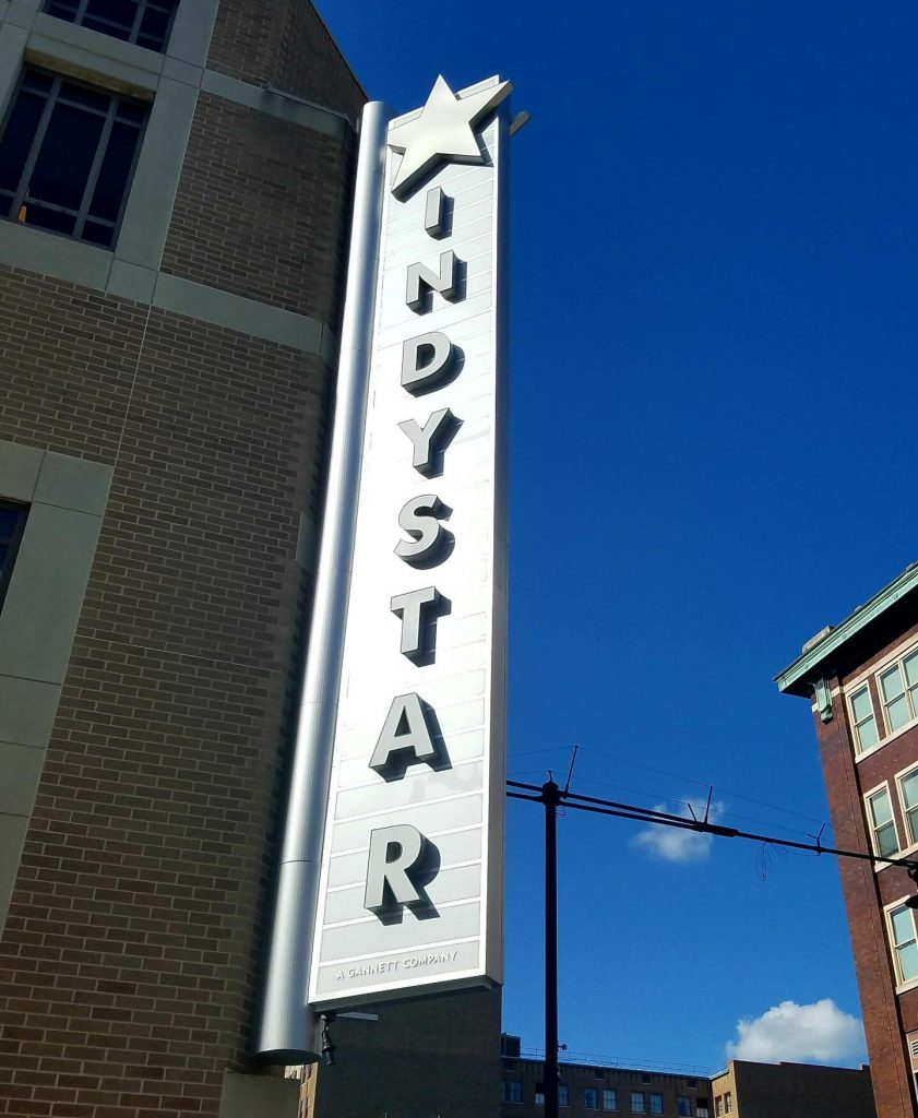 A close up view of a vertical marquee on the side of a building. It reads "IndyStar" and has a star at the top of it.