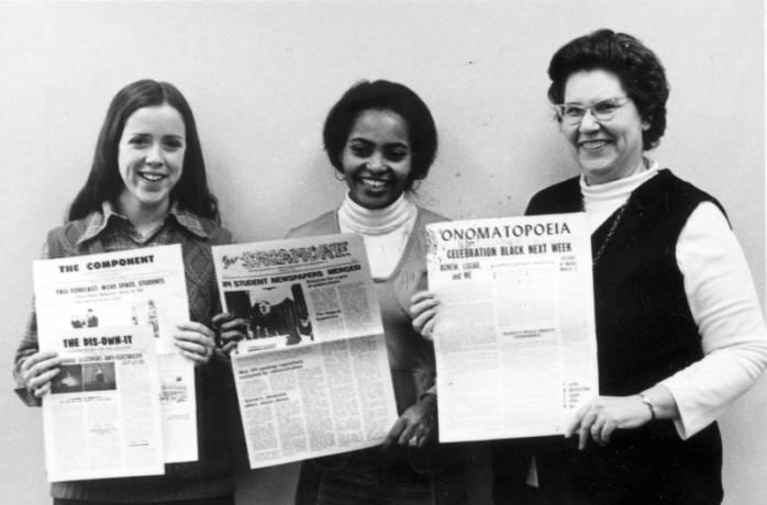 Three women hold up newspapers.