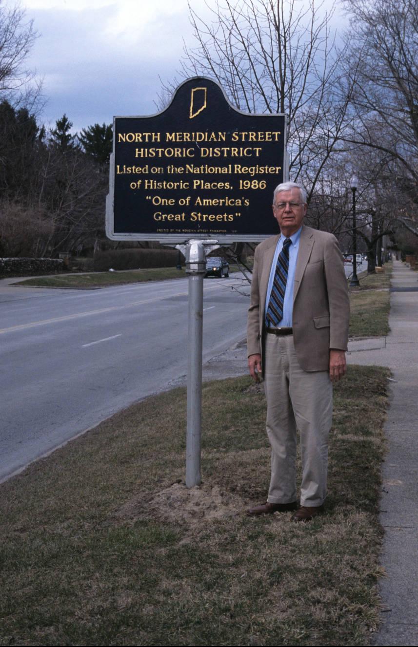A man stands next to a historical marker outside.