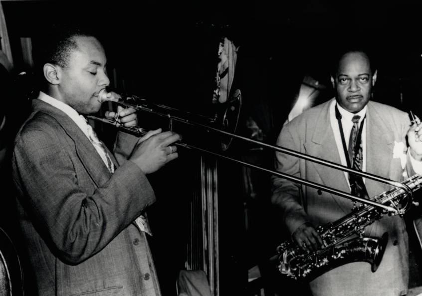 J. J. Johnson is playing trombone. Coleman Hawkins stands next to him holding a saxophone.