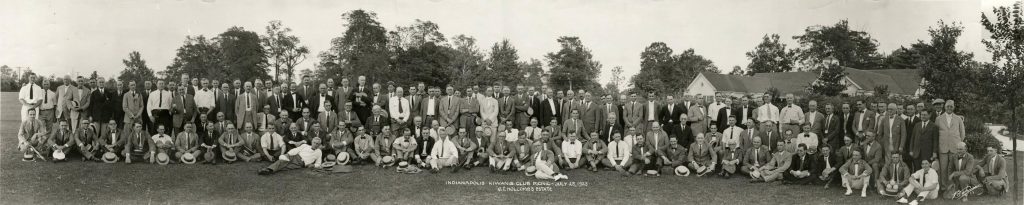 A large group of people gather together for a photograph in an open field behind a house.