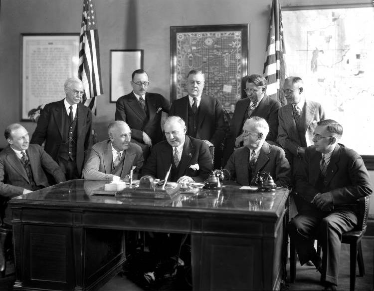 A group of men sit and stand behind a desk in an office space. 