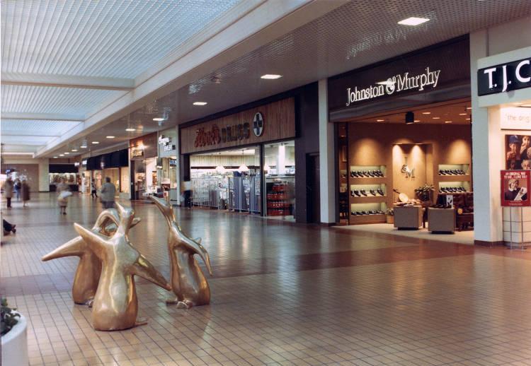 A sculpture of three gold penguins is in the middle of a mall corridor.