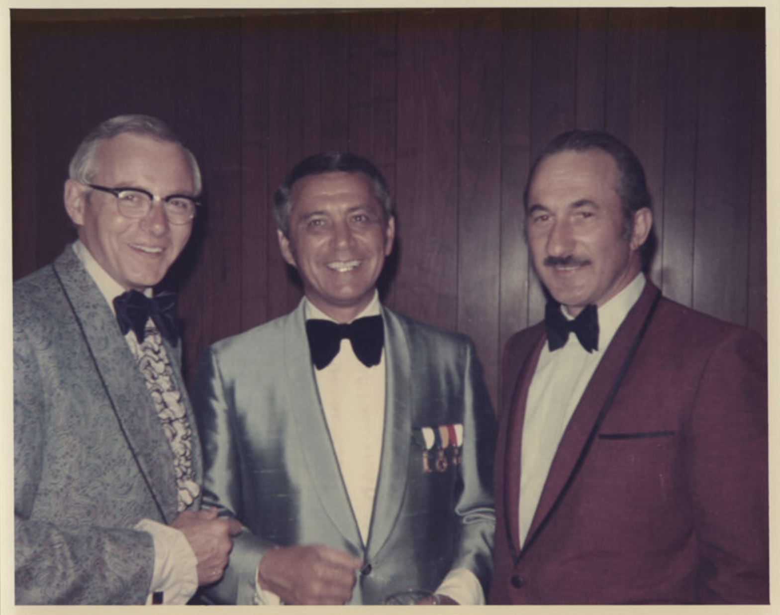 Three men, in evening wear with bow ties, are standing together.