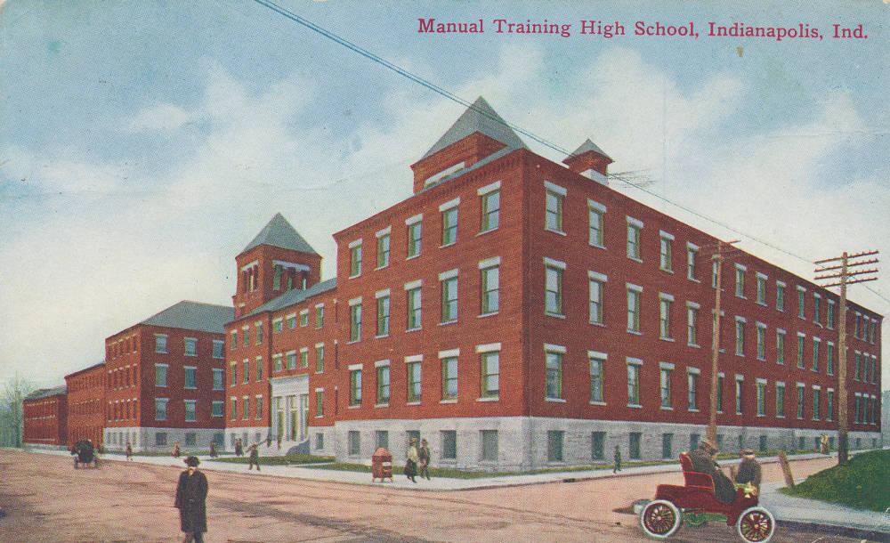 The school is a large four-story brick building with a limestone base and trim and two peaked towers on the roof.