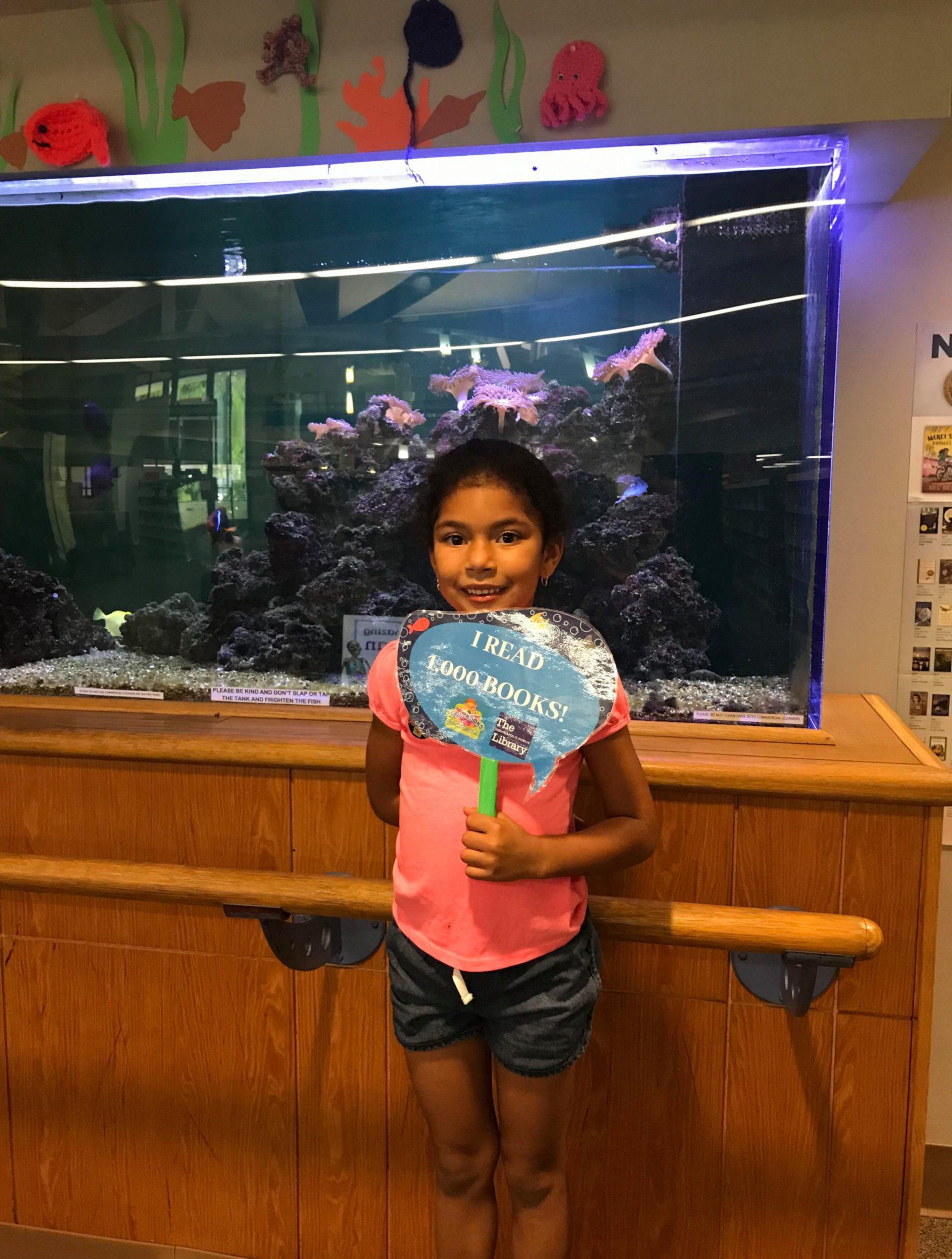 A child holds up a sign that reads "I read 1000 books!"