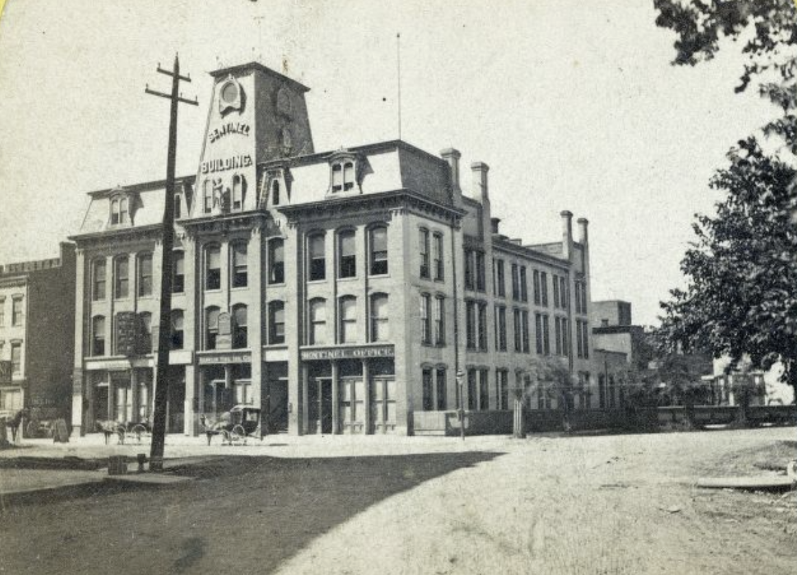 A four-story, Second Empire, stone building. It has a central tower (with "Sentinel Building" on it) at the front of the mansard roof.