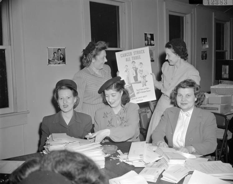 Little Red Door workers prepare a mailing and display a poster from the American Cancer Society.
