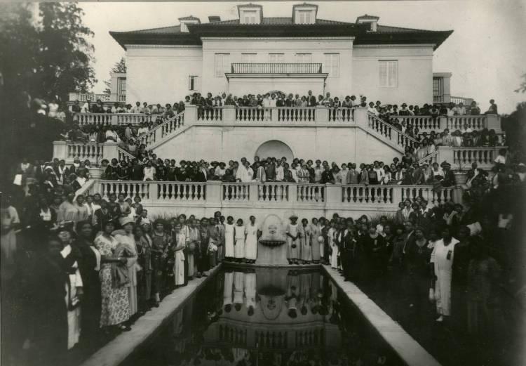 Convention attendees are posed around the reflecting pool at Villa Lewaro. People are also posed on both levels of an outdoor terrace. 