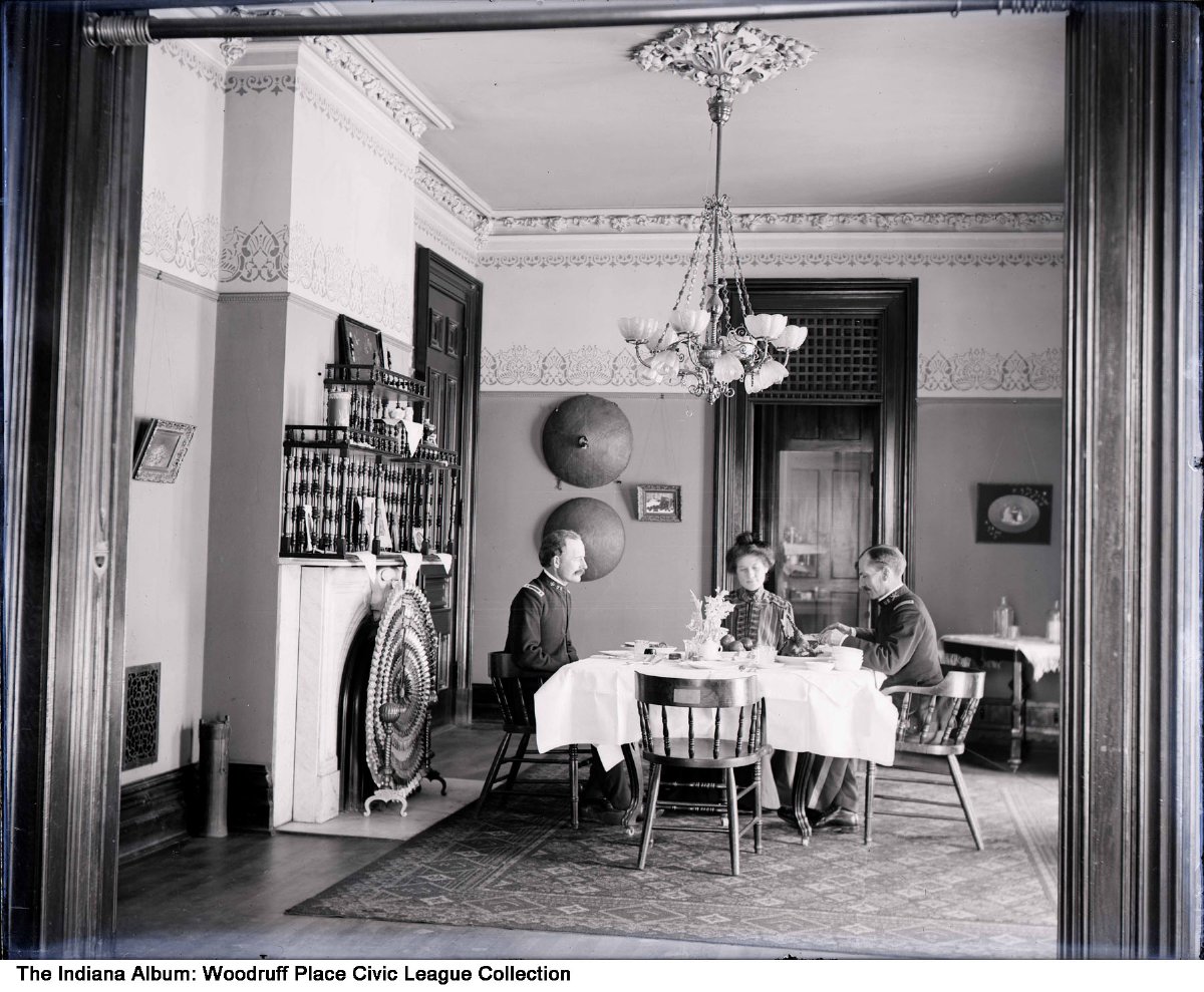 Two Military men and a woman sit at a dining table inside a home. 