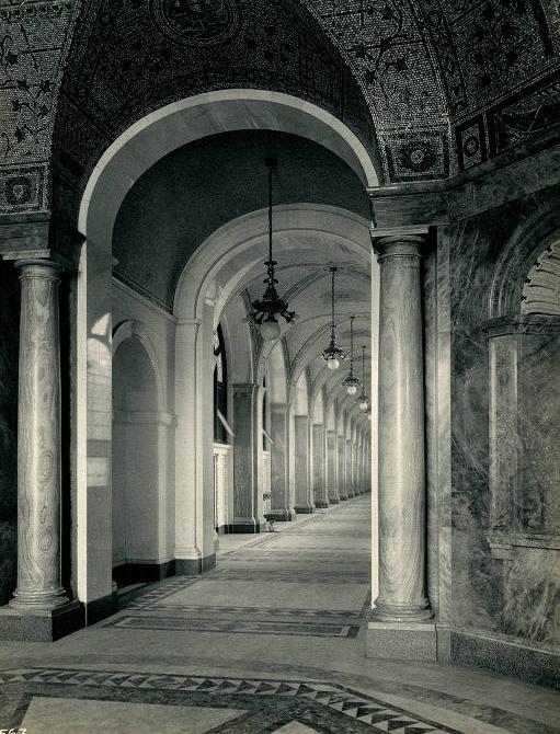 A long hallway of stone arches leads from a dome-ceilinged room with marble columns and gilded decorations.