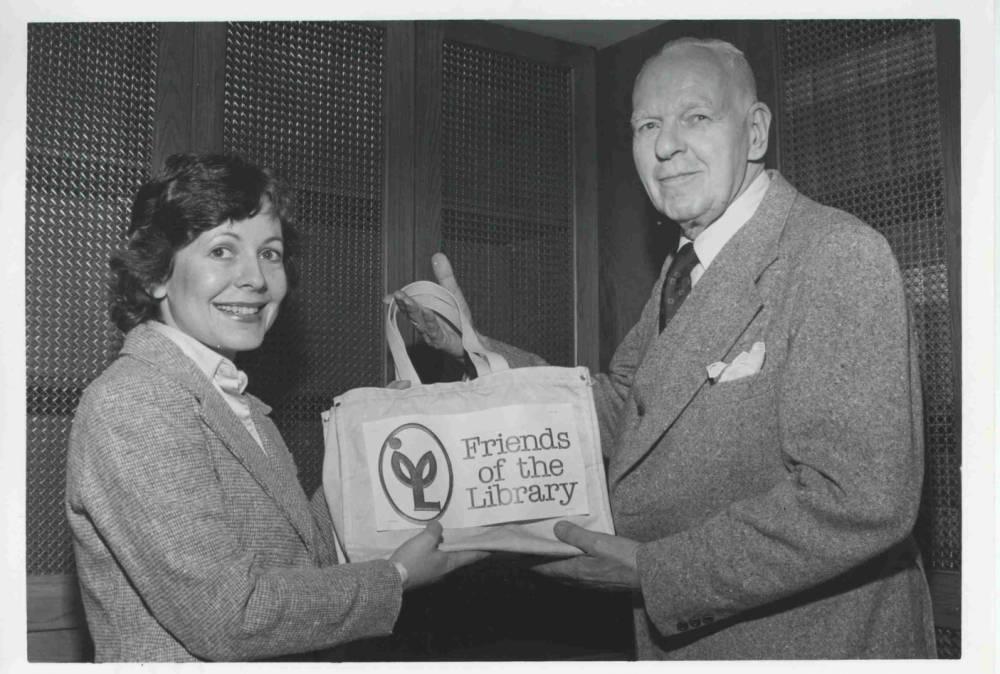 A woman and a man hold up a tote bag with a graphic on it that reads "Friends of the Library."