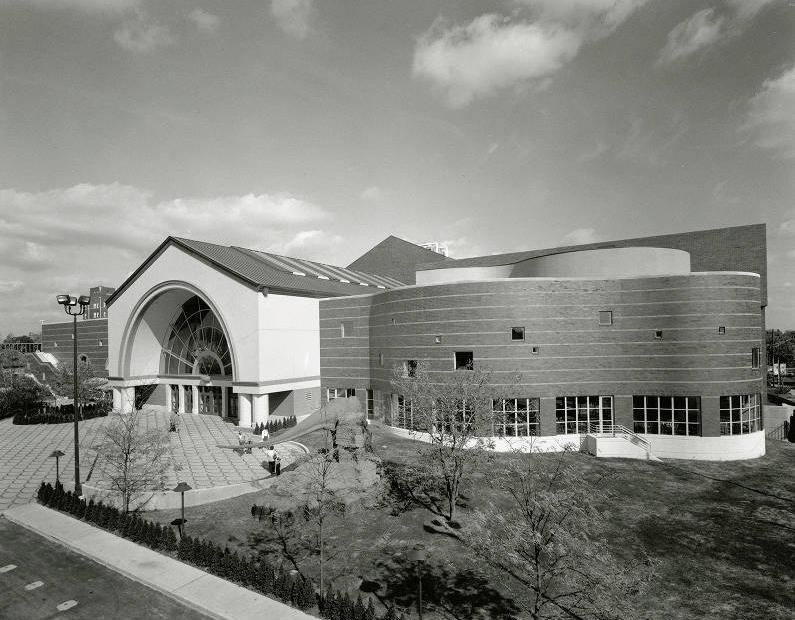 A large, modern, irregularly-shaped building with a glassed entryway under an arched opening.