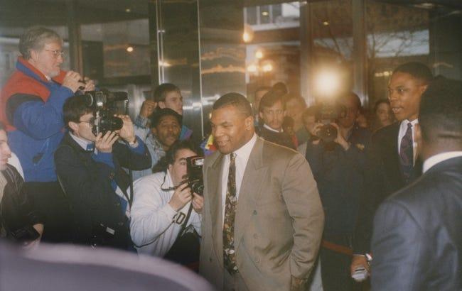 Mike Tyson stands outside and is surrounded by photographers.
