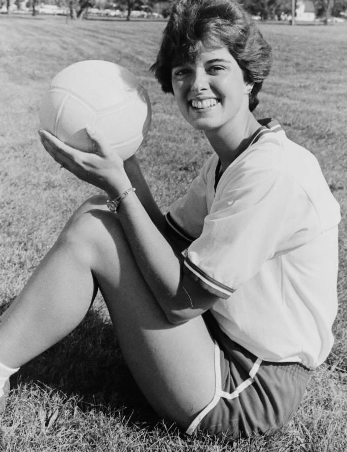 A woman sits on the ground and holds up a volleyball.