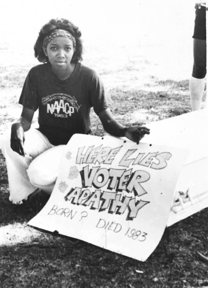 A woman sits and poses with a poster.