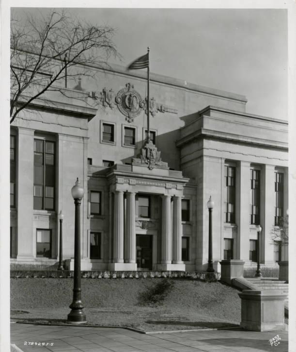 A long, stone, three-story neoclassical building with a centrally-place columned entry.