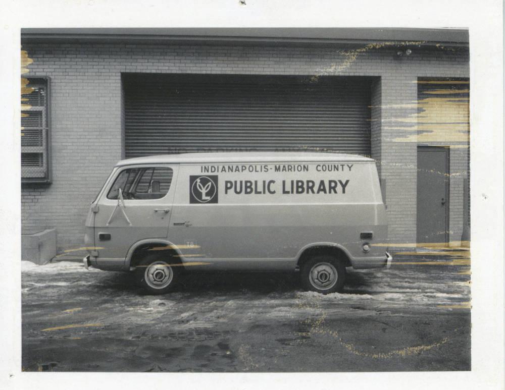 A van is parked outside a building. The van has a library logo on it.