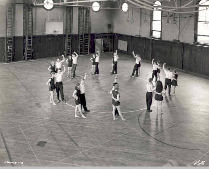 A group of people stand in a circle in the middle of a large gymnasium.