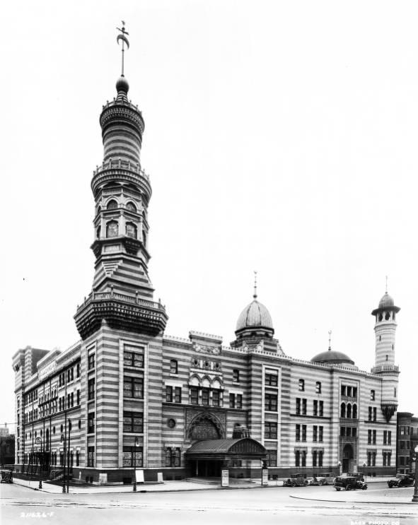 Exterior view of a multi-story building with elements of Middle Eastern and Egyptian architecture, including brick banding and minarets.