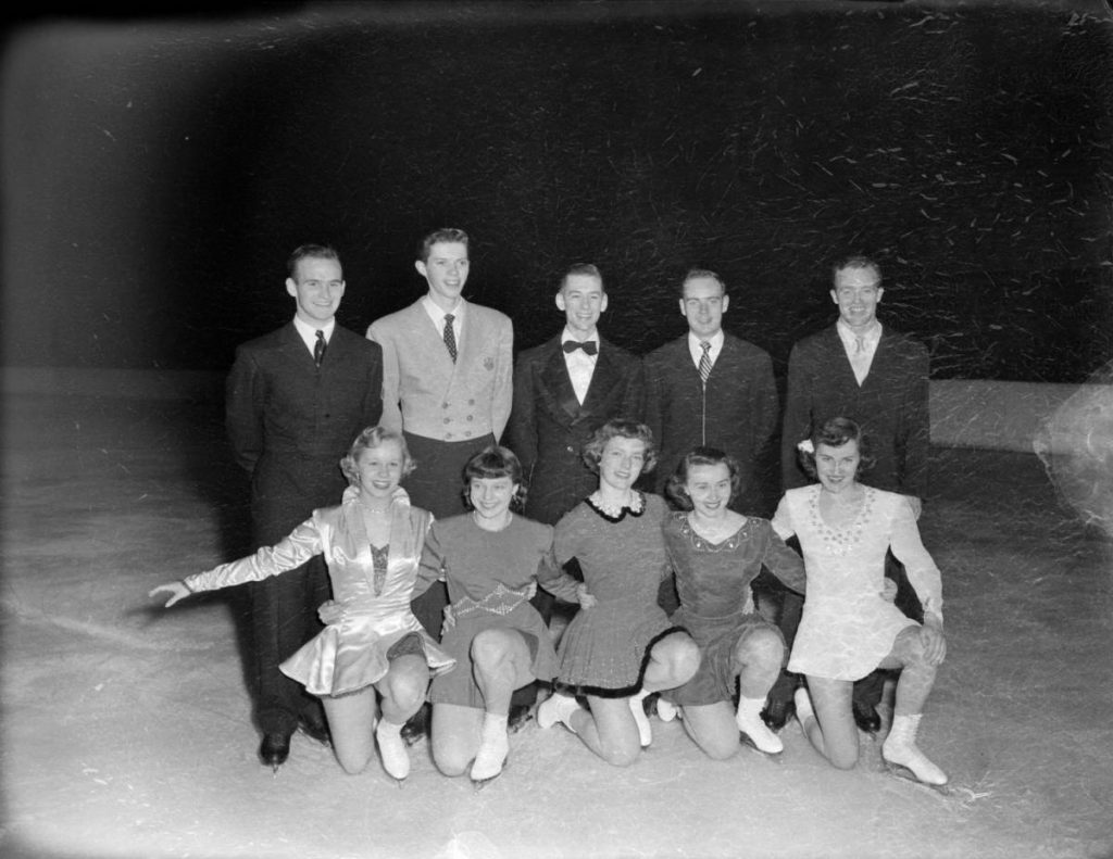 Five men and five women pose for a group portrait. They are all wearing ice skates and standing on an ice rink.