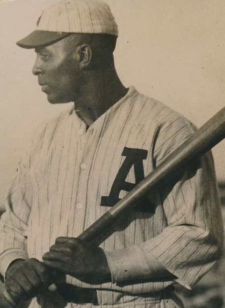 A man wearing a baseball uniform holds a bat.