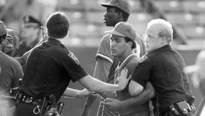Two police officers restrain a man on a baseball field.